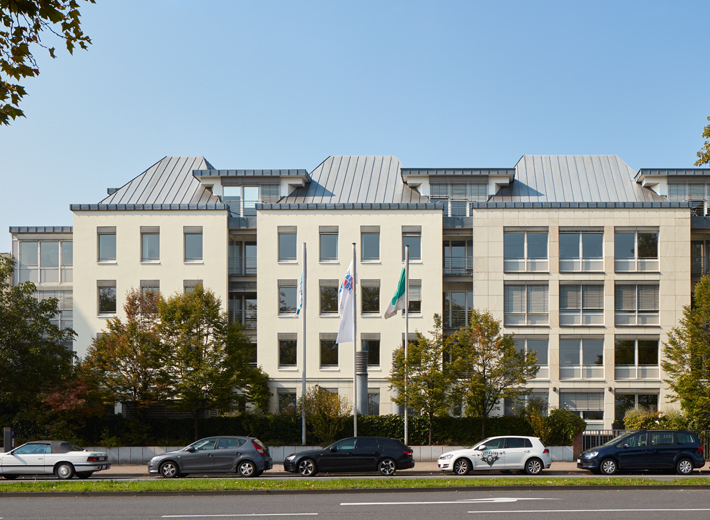 Hausfassade mit Straße im Vordergrundgrund, darauf Parken fünf Autos